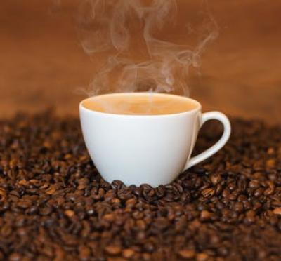 cup of steaming coffee surrounded by countless coffee beans