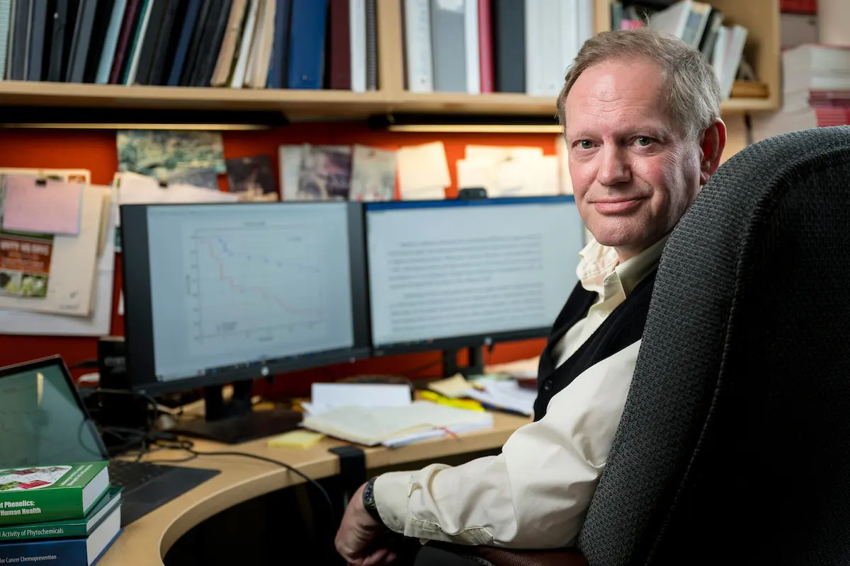 Dr. Fred Stevens seated at a desk in an office with dual monitors and books