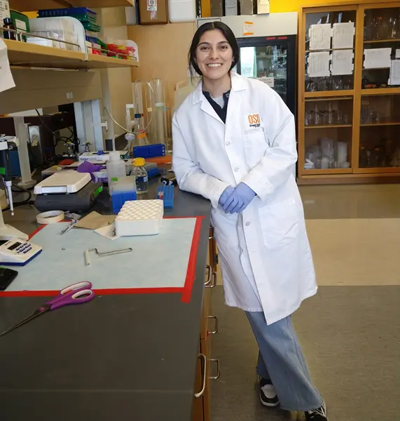 Nadia Gonzalez, wearing a white lab coat and purple gloves, posing for a photo in a wet lab