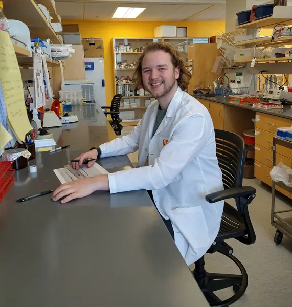 Tepary Cooley, wearing a white lab coat, posing for a photo in a wet lab